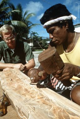 Steelworker 1ST Class Marion D. Jones watches as a local carver creates a storyboard on the island of Yap. Jones is a United States (US) Navy construction battalion member assigned to a Civic Action Team deployed to the area to aid villagers with construction projects and offer vocational training