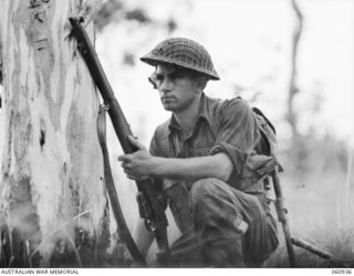 DONADABU AREA, NEW GUINEA. 1943-11-30. QX36436 PRIVATE E. D. THAMM OF NO 7 PLATOON, 2/10TH AUSTRALIAN INFANTRY BATTALION TAKES COVER BEHIND A TREE DURING COMBINED MANOEUVRES WITH THE 2/4TH ..