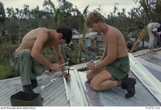 Informal outdoor portrait of Sapper Geoffery Maxwell (left) and Sapper Ted Cherry (right) finishing off a roof repair at Pangi village, Lifuka Island. This image relates to the service of Michael ..