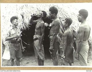 DUMPU, NEW GUINEA. 1944-01-04. MAKU A PAPUAN "DOCTOR BOY" GIVING MEDICINE TO SICK MARKHAM VALLEY MEN OUTSIDE THE DISPENSARY. MAKU CAN READ, WRITE AND SPEAK GOOD ENGLISH, AND READS WHAT TREATMENT ..