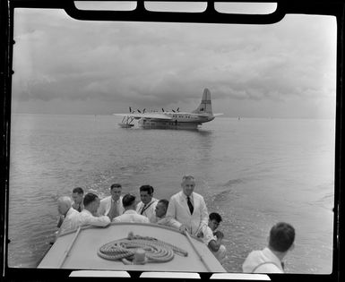 TEAL (Tasman Empire Airways Limited) ZK-AMM flying boat in background as unidentified passengers head to shore in Samoa