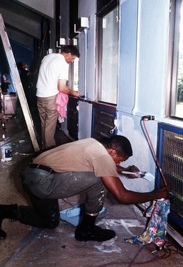 Sailors from the tank landing ship USS RACINE (LST-1191) paint the interior walls of a hospital ward, one of several civic action projects undertaken by the vessel's crew members