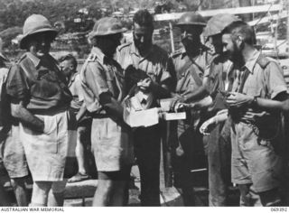 Port Moresby, New Guinea. 1942-04-12. Four officers from Lark Force of the Rabaul Garrison, receiving a tobacco issue on their arrival at Port Moresby aboard the HMAS Laurabada which successfully ..