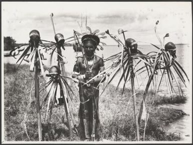 Village head man standing with skulls impaled on posts facing the river as a sign of hospitality, Kerewa village, Goaribari Island, Papua New Guinea, December 1922 / Frank Hurley
