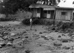 Francis Parker Shepard, from Scripps Institution of Oceanography, inspecting the damage to a house and scarp formation, at Kainalu, Molokai, after a tsunami. A scarp formation is displacement of the land surface by movement along the fault of an earthquake line and mass wasting caused by water runoff. April 1946