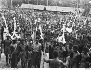 SONG RIVER, FINSCHHAFEN AREA, NEW GUINEA. 1944-03-26. ALL NATIVES GATHERED AROUND WHILE THEIR CHOIR SAND "NEARER MY GOD TO THEE", AND "GOD SAVE THE KING", IN ENGLISH, DURING FESTIVITIES HELD AT THE ..