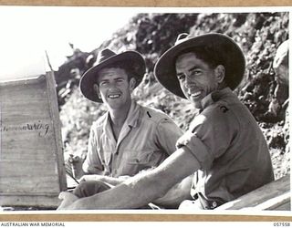 SALAMUA, NEW GUINEA. 1943-09-19. SX13471 SERGEANT G. R. MAINWARING, AUSTRALIAN WAR ARTIST, MILITARY HISTORY SECTION (LEFT) WORKING FROM A POSITION OVERLOOKING THE HARBOUR, WHILE QX44798 WARRANT ..