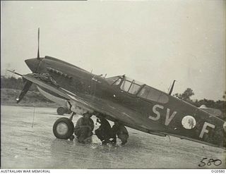 KIRIWINA, TROBRIAND ISLANDS, PAPUA. C. 1944-02. GROUND CREW OF NO. 76 (KITTYHAWK) SQUADRON RAAF TAKE SHELTER FROM THE RAIN IN ONE OF THE SUDDEN TROPICAL DOWNPOURS UNDER THE WING OF THE AIRCRAFT, ..