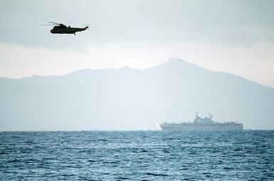 A British Royal Navy Sea King anti-submarine helicopter conducts screening operations for the amphibious assault ship USS SAIPAN (LHA 2) during NATO Exercise NORTHERN WEDDING 86. The mountains of Vestfjord, Norway, are in the background