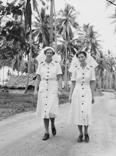 MADANG, NEW GUINEA. C. 1945. 500147 SENIOR SISTER E. DOHERTY (LEFT) AND 501159 SISTER B. FUREY, OF NO. 1 MEDICAL RECEIVING STATION RAAF IN THEIR DAY UNIFORMS RETURN TO THEIR QUARTERS FROM DUTY