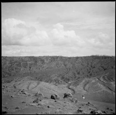 European man walking amongst piles of pumice and ash, Rabaul, New Guinea, 1937 / Sarah Chinnery