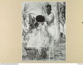 ALEXISHAFEN, NEW GUINEA. 1944-05-11. A CAPTURED JAPANESE RICE COOKING CAULDRON BEING USED AS A BATH TUB BY MEMBERS OF THE 35TH INFANTRY BATTALION, 8TH INFANTRY BRIGADE. PERSONS SHOWN ARE:- NX120436 ..