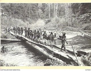 Papua, New Guinea. 1942-09. Men of the 2/33rd Australian Infantry Battalion crossing the Brown River on their way from Nauro to Menari. This huge tree that they are walking along, is the bridge ..