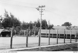 A barbed wire fence surrounds a caged area of the RAN War Criminal Compound at an RAN shore base where Japanese prisoners were held. The building in the background is the cafeteria. Work on this ..