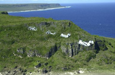 Two UH-46 Sea Knights and three UH-60 Black Hawk helicopters assigned to Andersen Air Force Base (AFB), fly over Guam near the Pacific Ocean coastline