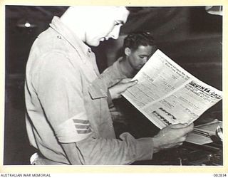 LAE AREA, NEW GUINEA. 1944-11-12. STAFF SERGEANT M.A. BARR, AT 8.30 PM READS A COPY OF THE ARMY NEWSPAPER 'GUINEA GOLD', THE FIRST SHEET OFF THE PRESS CARRYING TWO BLOCKS OF MELBOURNE CUP PICTURES ..