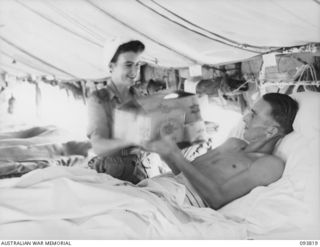 CAPE WOM, WEWAK AREA, NEW GUINEA, 1945-07-05. SISTER C. LEAHY AUSTRALIAN ARMY NURSING SERVICE (1), GIVING PRIVATE W.J. SUTHERLAND (2), A PATIENT AT 104 CASUALTY CLEARING STATION, A MID-YEAR HAMPER ..