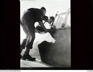 NADZAB, NEW GUINEA. C. 1944-02. SERGEANT C. J. MCFARLANE, COOPAROO, QLD (IN COCKPIT) DISCUSSING THE ENGINE NOTE WITH SERGEANT D. H. PAVLICH, PORT PIRIE, SA (ON WING) AS THEY RUN UP THE MOTOR OF A ..