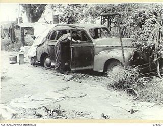 HANSA BAY, NEW GUINEA. 1944-06-22. WX38253 LANCE CORPORAL M.R. WEIR, 4TH INFANTRY BATTALION, INSPECTING A BURNT OUT JAPANESE STAFF CAR