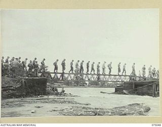 LAE, NEW GUINEA. 1944-08-09. AUSTRALIAN AND AMERICAN TROOPS CROSSING THE FIRST SPAN OF THE NEW BRIDGE ACROSS THE BUTIBUM RIVER WHICH IS BEING BUILT BY THE 20TH FIELD COMPANY, TO REPLACE THE OLD ..