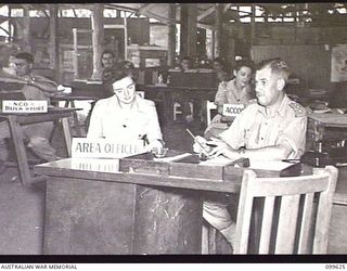 LAE, NEW GUINEA, 1946-01-11. CORPORAL D. M. O'CONNELL (1) AND CAPTAIN W. A. E. SPROTT, AREA OFFICER (2) WORKING IN THE OFFICE OF AUSTRALIAN ARMY CANTEENS SERVICE BULK STORES