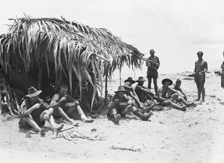 PONGANI, NEW GUINEA. 1942-10. MEMBERS OF 2/6TH AUSTRALIAN INDEPENDENT COMPANY GATHER IN THE SHADE OF A CRUDE NATIVE SHELTER WHILE THEY PARTAKE OF RATIONS. SHOWN ARE: TROOPER (TPR) D. BARDON (1); ..