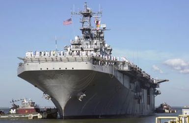 The Tarawa Class Amphibious Assault Ship USS SAIPAN (LHA 2) guided to the pier by tugboats as her Sailors man the rails. The SAIPAN returned to Naval Station (NS) Norfolk, Virginia (VA), after completing a three-month surge deployment in support of the Global War on Terrorism (GWOT)