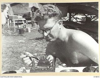 1943-05-07. NEW GUINEA. MILNE BAY. LAC W. SIMPSON OF UNLEY, SOUTH AUSTRALIA, PUTS THE FINISHING TOUCHES TO AN INKWELL HE MADE OUT OF JAPANESE BULLETS AND WOODEN SOUVENIRS. (NEGATIVE BY N. BROWN)