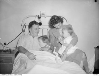 HEIDELBERG, VIC. 1944-01-15. SERGEANT E. G. SAUNDERS, A WOUNDED SOLDIER EVACUATED FROM NEW GUINEA, CUDDLES HIS YOUNG DAUGHTER BEVERLY WHILE HIS WIFE NURSES BABY DENISE WHEN THEY VISIT HIM IN THE ..