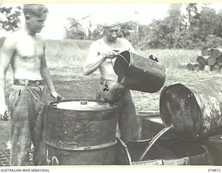 LAE-NADZAB, NEW GUINEA. 1944-07-20. PRIVATE R.D. WALKLEY (1) AND PRIVATE A. CLARKE (2) OF THE 2ND CORPS SALVAGE UNIT FILLING 44 GALLON DRUMS WITH USED ENGINE OIL FOR SHIPMENT BACK TO THE MAINLAND ..