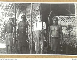 ULUGUDU, NEW GUINEA, 1943-10-25. REVEREND JOHANN DEKKER, LUTHERAN MISSIONARY WITH HIS NATIVE BOYS IN A HUT WHICH HE BUILT IN THE JUNGLE TO ESCAPE THE ALLIED BOMBING RAIDS