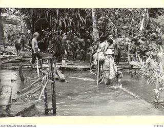 1943-01-22. PAPUA. ALLIED TROOPS ON THE MOVE FROM BUNA TO SANANANDA FORD A MUDDY RIVER CROSSING WITH THE AID OF NATIVE PAPUAN BEARERS