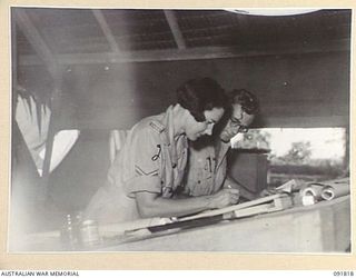 LAE, NEW GUINEA, 1945-05-15. CORPORAL C.J. LOCK (1), INTELLIGENCE, HQ FIRST ARMY, GIVING INSTRUCTIONS TO CPL M.H. HAMMOND (2), IN HER NEW JOB. A FEW DAYS AFTER THEIR ARRIVAL FROM AUSTRALIA AWAS ..