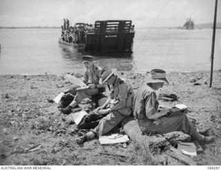 MALAGUNA MISSION, NEW BRITAIN. 1945-09-10. WAR CORRESPONDENTS TYPING THEIR STORIES ON THE BEACH DURING THE FIRST DAY OF OCCUPATION OF THE RABAUL AREA BY TROOPS OF 4 INFANTRY BRIGADE. IDENTIFIED ..