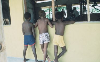 Native children look on at a construction site at Port Vila as members of Naval Mobile Construction Battalion 62 help repair damage caused by Cyclone Uma