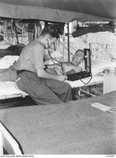 LAE. NEW GUINEA. 1944-07-14. NX171725 CAPTAIN W. HEMPHILL, MEDICAL OFFICER (1), TESTING THE BLOOD PRESSURE OF VX124117 PRIVATE J.P. BOURKE (2) IN ONE OF THE TENT WARDS OF THE 2/7TH AUSTRALIAN ..