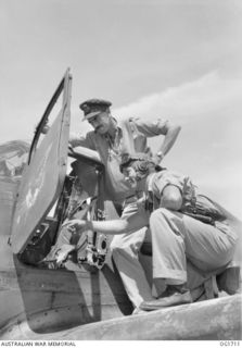 TADJI NEAR AITAPE, NORTH EAST NEW GUINEA. C. 1944-09. US AIR FORCE PILOT (KNEELING) EXPLAINS THE INSTRUMENT PANEL OF HIS AIRACOBRA FIGHTER AIRCRAFT TO SQUADRON LEADER W. HAMBLIN, COMMANDING OFFICER ..