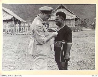TOROKINA, BOUGAINVILLE, 1945-08-04. LIEUTENANT-GENERAL S.G. SAVIGE, GENERAL OFFICER COMMANDING 2 CORPS (1), AT THE AUSTRALIAN NEW GUINEA ADMINISTRATIVE UNIT NATIVE COMPOUND PRESENTING A VALOUR ..