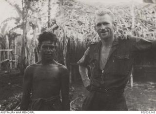 Kokoda Track, Papua. 1942. Informal portrait of NX239 Captain Bruce Brock and an indigenous (native) boy, Effogi, outside a thatched hut. (Original housed in AWM Archive Store)