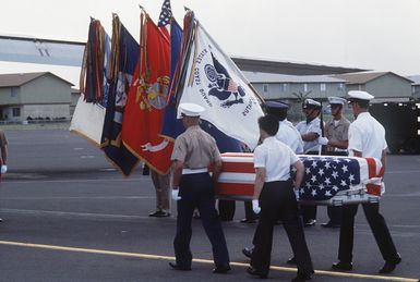 A combined services Color Guard stands by as pallbearers carry the flag-draped casket of a former MIA to a C-141 Starlifter aircraft during a ceremony on the flight line. Eleven former MIA's returned from Vietnam are being airlifted to Travis Air Force Base, Calif