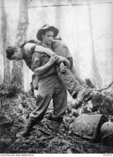 1943-07-30. MOUNT TAMBU, NEW GUINEA. 2/5TH BATTALION STRETCHER BEARER CORPORAL LESLIE (BULL) ALLEN MM, AGE 26, OF BALLARAT, VIC, CARRYING TO SAFETY AN AMERICAN SOLDIER WHO HAD BEEN KNOCKED ..
