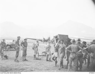 DUMPU, NEW GUINEA. 1944-01-08. NATIVES AT DUMPU AIR STRIP UNLOADING PART OF A FOWLER'S STOVE BELONGING TO 15TH FIELD AMBULANCE. THE ONLY MEMBER OF THIS UNIT PRESENT IS SHOWN ON THE EXTREME LEFT. HE ..