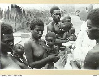 BOUGAINVILLE ISLAND. 1944-12-24. QX42595 CHAPLAIN J.P. MCMANUS, 2/1ST AUSTRALIAN GENERAL HOSPITAL CHRISTENING NATIVE BABIES OF THE KIETA TRIBE FROM THE GUAVA VILLAGE AT THE AUSTRALIAN NEW GUINEA ..