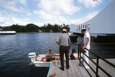 A Navy chaplain stands by as members of the U.S. Park Service tie up a small boat at the USS ARIZONA Memorial prior to taking part in a memorial service for a crew member of the battleship USS ARIZONA (BB-39). During the service, a canister containing the crew member's remains will be dropped into an opening in the Arizona's sunken hull, thus committing them to the submerged vessel