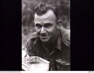 BUKAUA, NEW GUINEA. 1943-10-18. PORTRAIT OF QX45103 LIEUTENANT S. E. HOME, OFFICER COMMANDING, NO. 11 PLATOON "B" COMPANY 29/46TH AUSTRALIAN INFANTRY BATTALION, HAVING A MIDDAY MEAL AT THE LUTHERAN ..