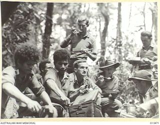 1942-10-19. A GROUP OF AUSTRALIAN INFANTRYMEN ON PATROL IN NEW GUINEA SNATCH A QUICK MEAL THAT HAS BEEN PREPARED BY THEIR NATIVE COOKS. (NEGATIVE BY PARER)