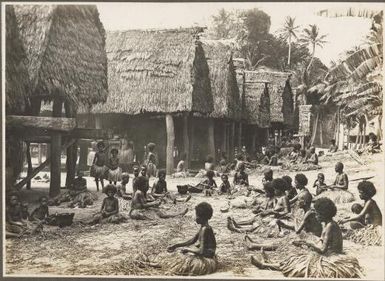 Scene in  Mailu Village, [women weaving in front of huts, Papua New Guinea]