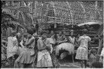 Mortuary ceremony, Omarakana: women by partially full yam house, one holds a skirt for ritual exchange