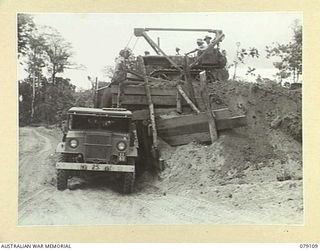 BOUGAINVILLE ISLAND. 1945-02-14. TROOPS OF THE 61ST INFANTRY BATTALION USING A SMALL BULLDOZER TO LOAD A TRUCK WITH SOIL FOR SURFACING A CORDUROY SECTION OF THE JABA SOUTH ROAD