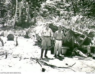 THE SOLOMON ISLANDS, 1945-10. A JAPANESE OFFICER AND HIS BATMAN WITH LEAN-TO ACCOMMODATION AT THEIR INTERNMENT CAMP. (RNZAF OFFICIAL PHOTOGRAPH.)